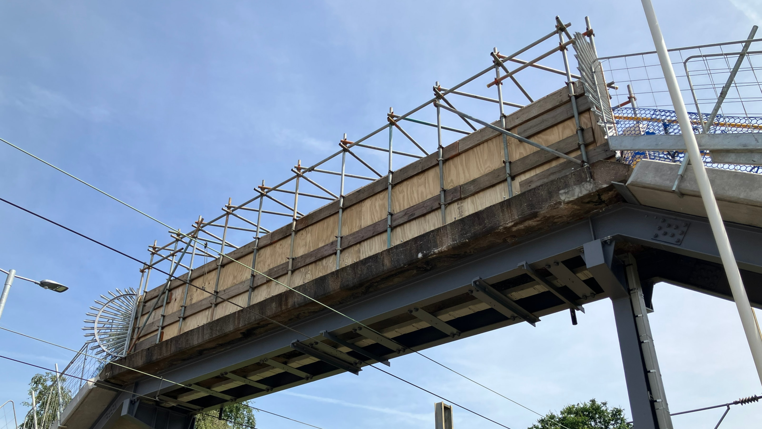 A steel pedestrian footbridge spanning electrified railway tracks at a station